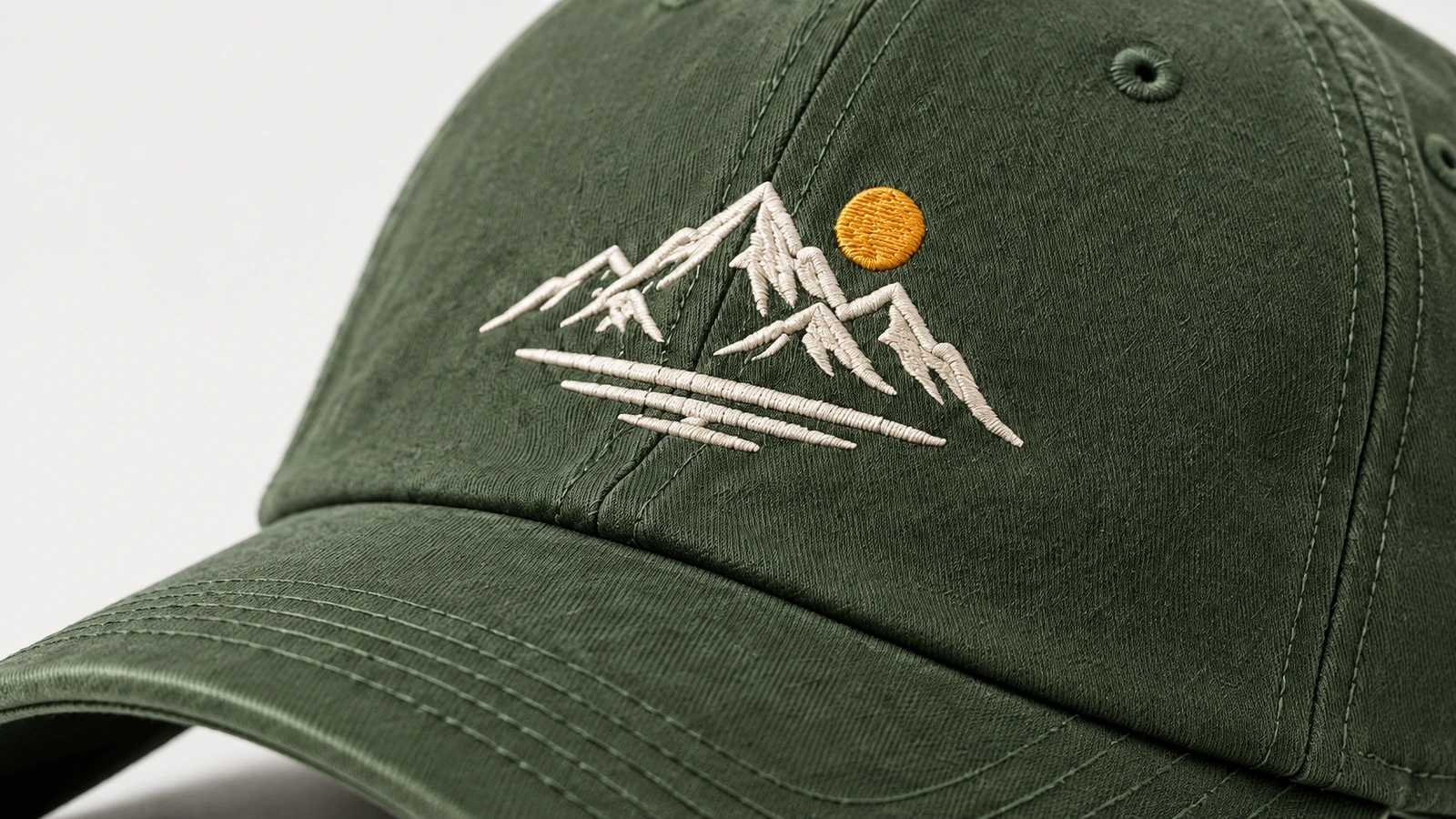 緑のキャップに施された白い山の刺繍と黄色い太陽のクローズアップ